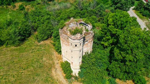 A drone shot of a water tower from 15th century surrounded by trees in green field