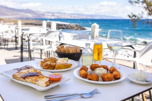A close-up shot of fried fast food and French toast on a white table with a background of a sea