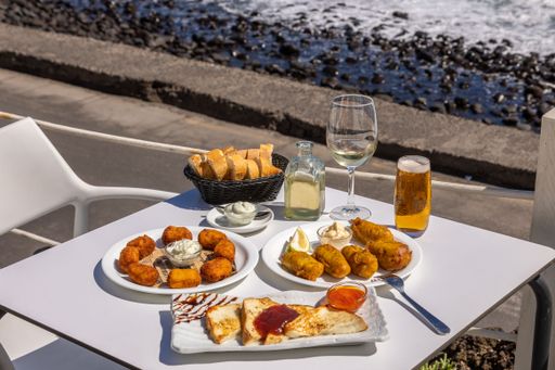 A close-up shot of fried fast food and French toast on a white table with a background of a beach