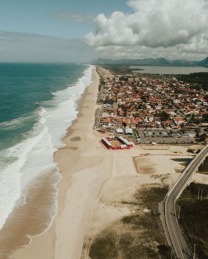 A vertical painting of a small town near a beach with cloudy sky