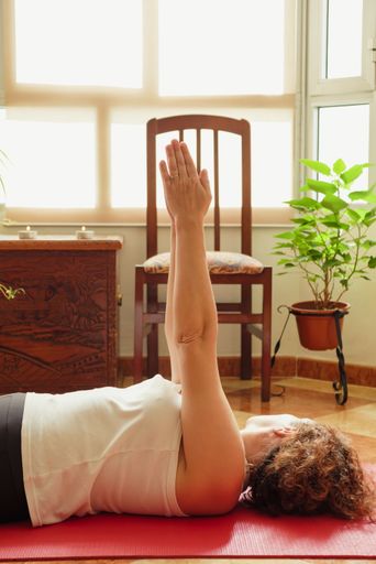 Stock photo of an unrecognizable redheaded woman practicing yoga at home during the pandemic lying on a red yoga mat
