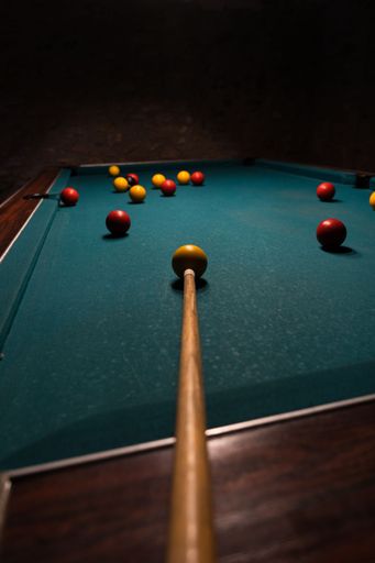 A vertical footage of a billiard table with balls and cue in a dark room