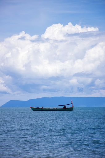 A vertical side view of small boat in the sea under blue cloudy sky