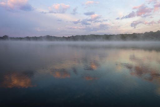 Fog lifts off the lake with dramatic cloudscape at sunrise creating a peaceful relaxing scene with copy space