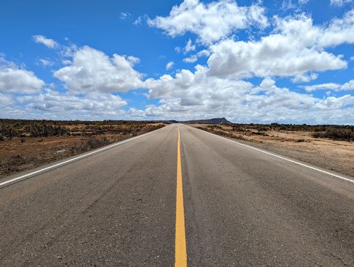 A beautiful view of an empty road with fields under the blue cloudy sky