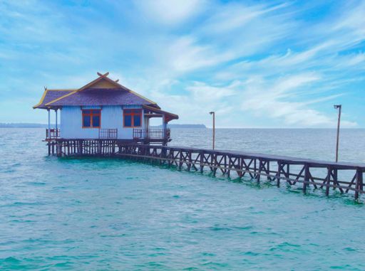 A scenic view of the house with pier in the sea on a sunny day