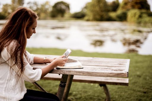 A closeup shot of a female sitting in the park while using her smartphone with a blurred background