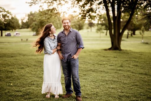 A beautiful shot of a couple standing in a grassy field while smiling with a blurred background