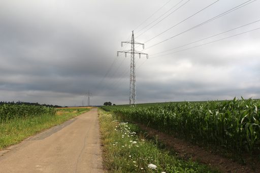 A road surrounded by greenery and transmission towers under a cloudy sky in the countryside