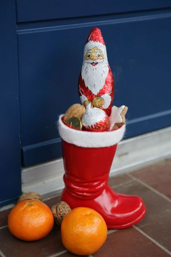 A vertical shot of a Santa Claus chocolate candy in a big red boot with mandarines