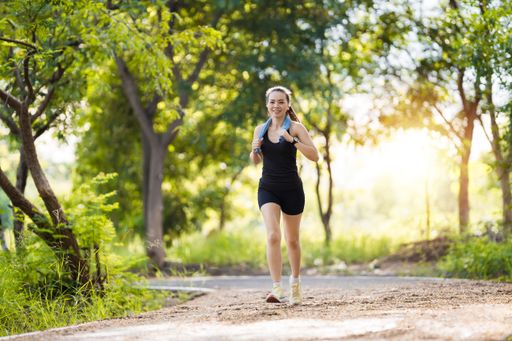 A fit Asian female jogging in a park in black sportswear surrounded by greenery