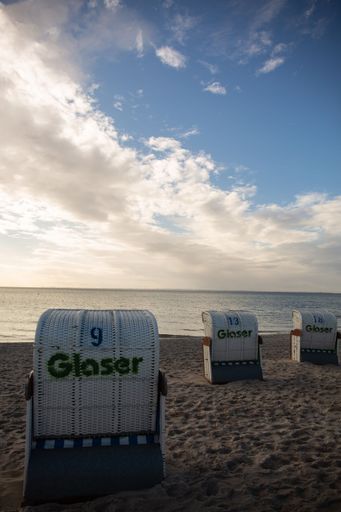 A vertical shot of white wicker beach chairs on a sandy beach under blue cloudy sky at sunset