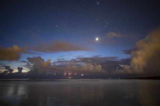 A beautiful shot of the beach and the fluffy clouds in the sky at night