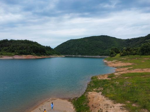 A beautiful small lake surrounded by green mountains against a blue cloudy sky