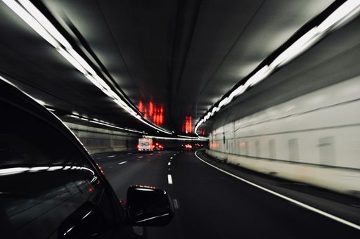 a black varnished car drives through a lighted tunnel at high speed