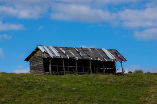 A scenic shot of an old abandoned hut on top of a green hill with a bright blue sky in the background