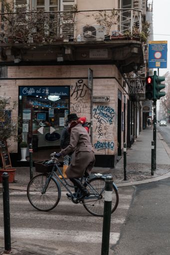 A vertical of a woman riding a bicycle in front of a cafe with graffiti on the narrow streets of Turin in winter