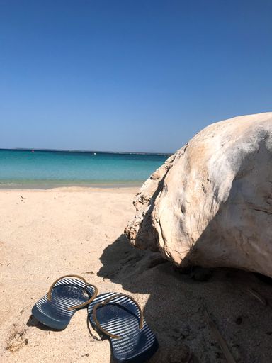 A vertical shot of sandals on the sand at the beach