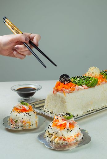 A vertical shot of a sushi cake, two pieces in plates, soy sauce and woman's hand holding chopsticks