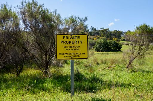 A sign with the text ''Private property'' isolated in a green field with trees under the clear sky