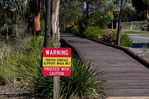 A warning sign by the wooden pathway surrounded by trees