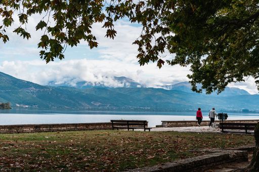 Beautiful cityscape view of Ioannina lake surrounded by mountains and green trees under fluffy clouds on summer day