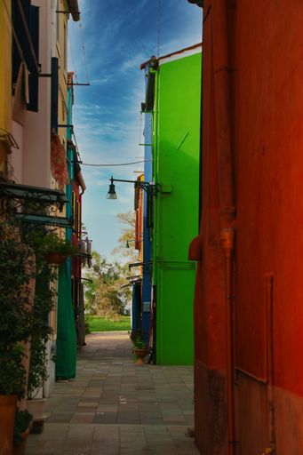 A vertical shot of narrow street with multicolored residential buildings under blue sky in Europe
