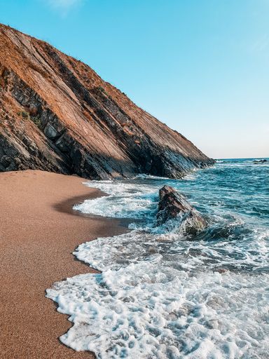A beautiful landscape of rocky cliffs on the seashore, blue waves crashing on sandy beach