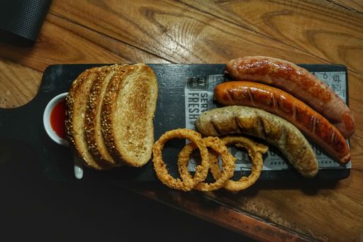 A closeup top view of bratwurst sausages with some onion rings, ketchup, and bread slices