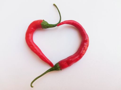 Two red chilies forming a heart on a white background