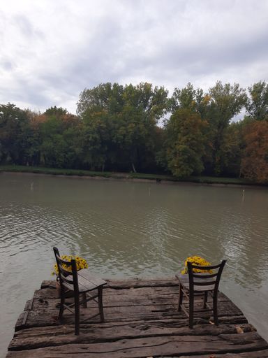 A vertical shot of two chairs with bouquets on an old pier over a dirty lake