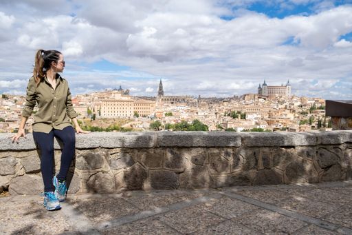 A young adult woman tourist sitting at the view looking at the city of Toledo in Spain