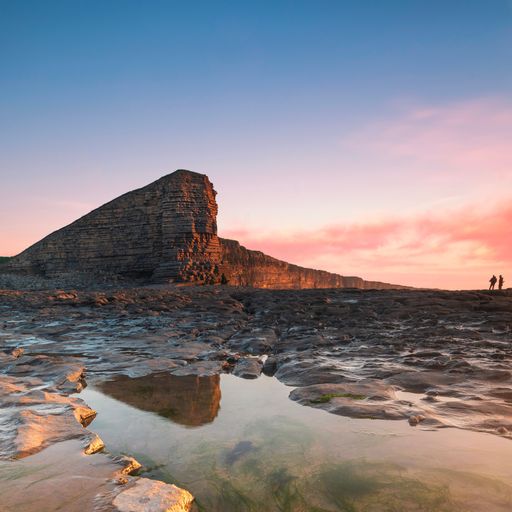 A mesmerizing hiking destination, a cliff and a pond with the silhouette of hikers captured at sunset
