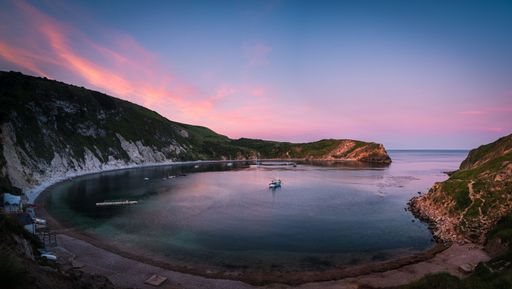A mesmerizing seascape displaying a sailing boat floating on the Lulworth Cove bay during sunset