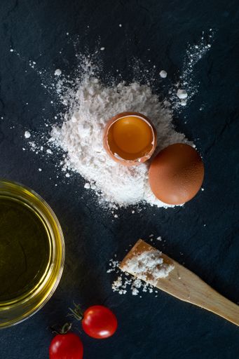 A flat lay of raw baking ingredients on black surface with wooden spatula