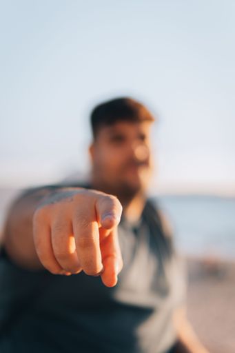 An out of focus of a  cool Caucasian man in a shirt and sitting and pointing at the camera