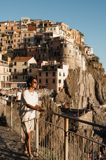 A young man overlooking the rocky coast against the village and cliff in Manarola, Cinque Terre, Italy
