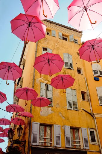A vertical shot of pink umbrellas hanging above a street in a Grasse, France