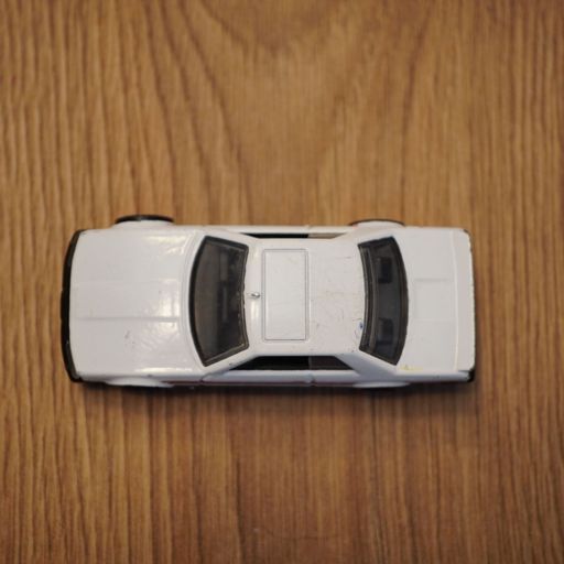 The top view of a white Mattel Hot Wheels toy car on a wooden surface