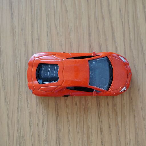 The top view of a red Mattel Hot Wheels toy car on a wooden surface