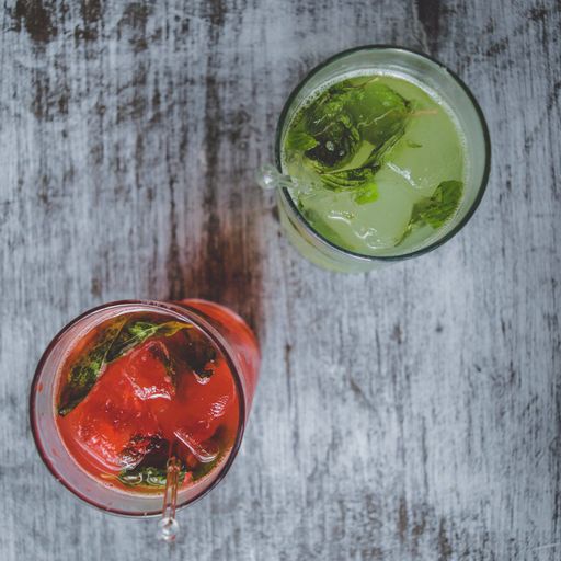 Two cocktails, one red and one green, 2x1, served on a rustic wooden table. It is a preparation based on a mixture of different beverages