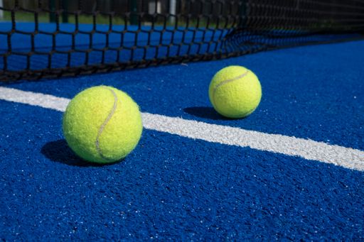 A closeup of two balls near the net of a paddle tennis blue court, racket sports