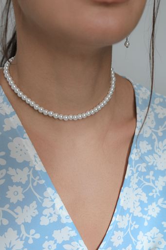 A vertical closeup of a pearl necklace around a Caucasian female's neck.