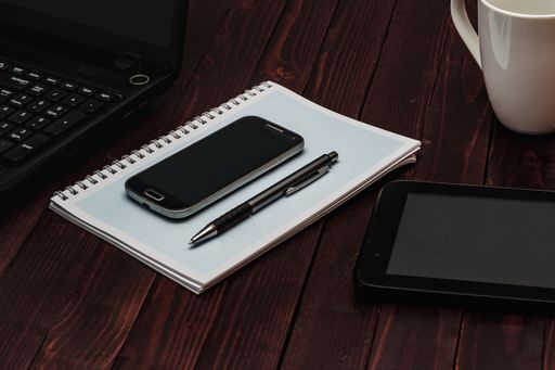 A high angle shot of a smartphone, a pen on an open notebook next to a tablet