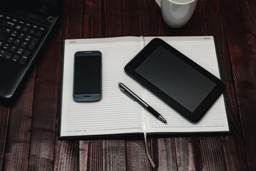 A high angle shot of a smartphone, a pen and a tablet on an open notebook