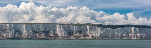 Amazing wide angle panoramic shot of the White Cliffs of Dover, a light house on top of the cliff. Beautiful fluffy clouds in the background.