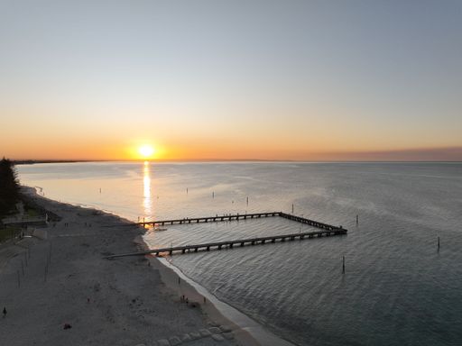 An aerial view of a long connected pier over the sea under orange sunset sky