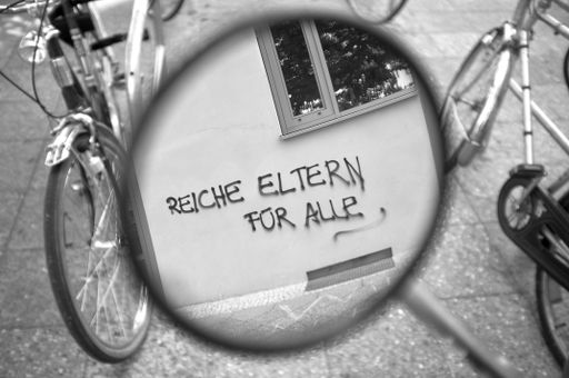 A graffiti on a wall of new residential building, demands in german rich parents for everyone. All of this, is seen in the backmirror of bicycle