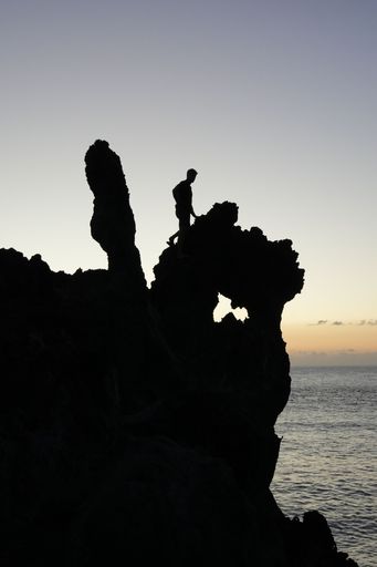 A vertical shot of a guy climbing the rocks on the seashore at sunset