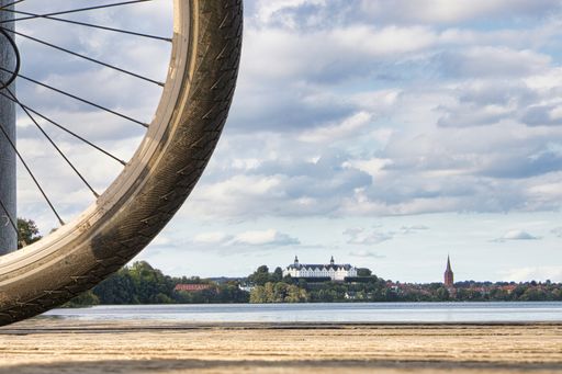 rear bike wheel in front of a panoramic shot of Ploner see (name of lake) background plon castle in Ploen, Germany